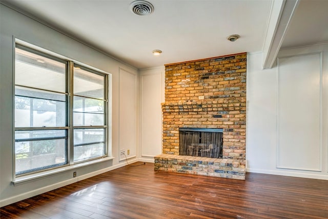 unfurnished living room with plenty of natural light, dark hardwood / wood-style flooring, crown molding, and a brick fireplace