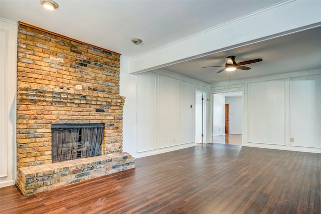 unfurnished living room featuring ceiling fan, ornamental molding, dark wood-type flooring, and a brick fireplace