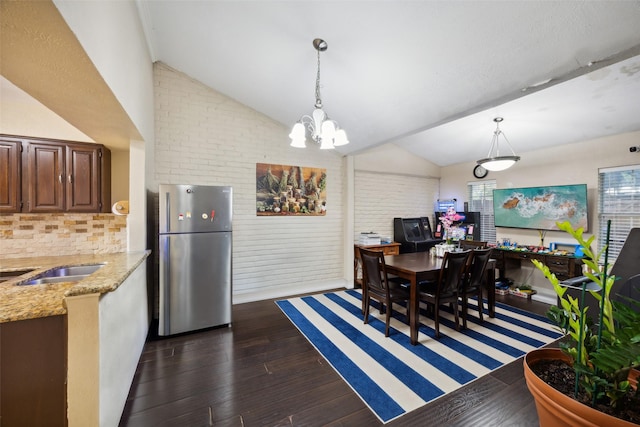 dining room with dark hardwood / wood-style flooring, an inviting chandelier, lofted ceiling, and brick wall