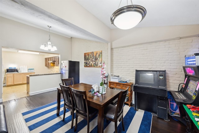 dining space featuring a chandelier, lofted ceiling, dark wood-type flooring, and brick wall