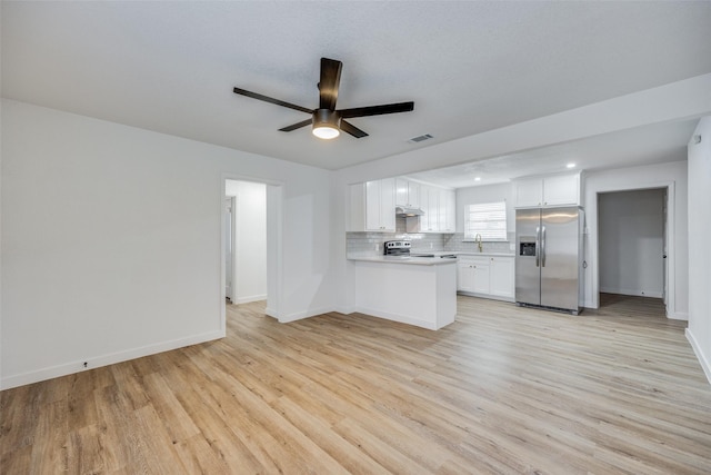 kitchen with light hardwood / wood-style flooring, appliances with stainless steel finishes, white cabinetry, decorative backsplash, and kitchen peninsula