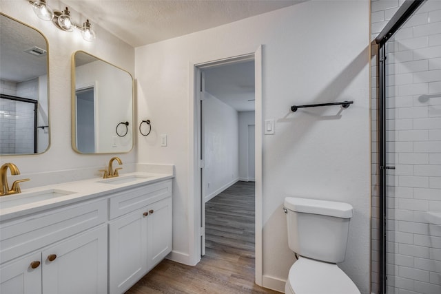 bathroom with vanity, a textured ceiling, wood-type flooring, toilet, and a shower with shower door