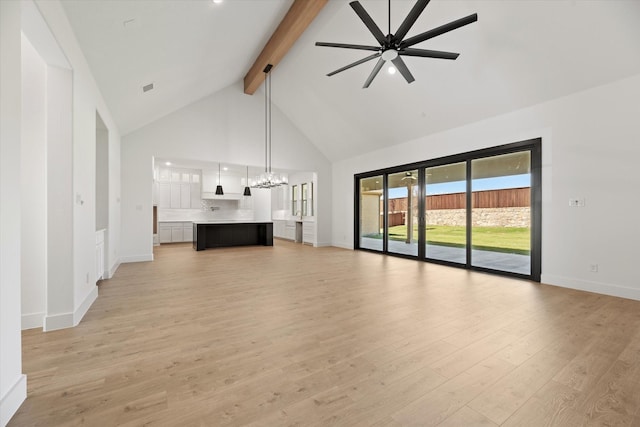 unfurnished living room with beam ceiling, ceiling fan with notable chandelier, light hardwood / wood-style floors, and high vaulted ceiling