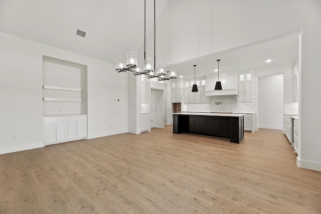 kitchen featuring built in shelves, pendant lighting, white cabinets, light hardwood / wood-style floors, and a large island