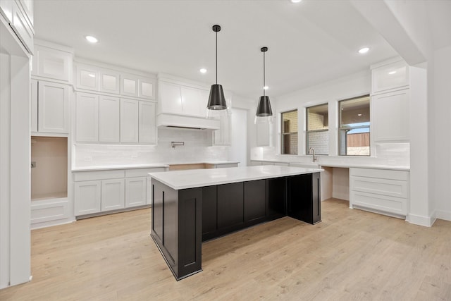 kitchen with light wood-type flooring, backsplash, sink, white cabinets, and a center island