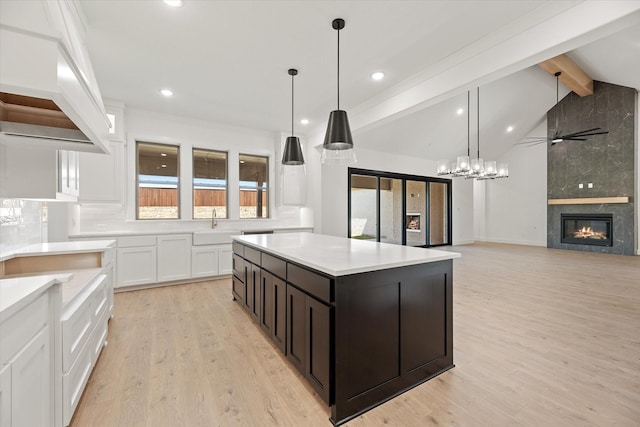 kitchen featuring a kitchen island, vaulted ceiling with beams, a tiled fireplace, white cabinets, and light wood-type flooring