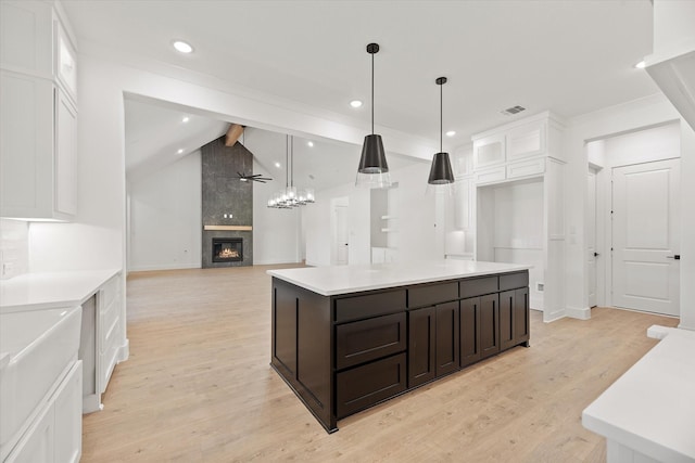 kitchen with a tile fireplace, white cabinets, light hardwood / wood-style flooring, vaulted ceiling with beams, and decorative light fixtures