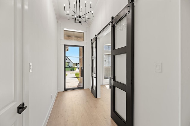 entryway featuring an inviting chandelier, crown molding, a barn door, a towering ceiling, and light hardwood / wood-style floors