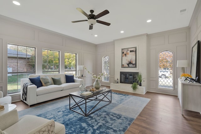 living room featuring wood-type flooring, a brick fireplace, ceiling fan, and a healthy amount of sunlight