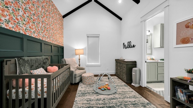 bedroom with ensuite bathroom, a crib, dark wood-type flooring, and high vaulted ceiling