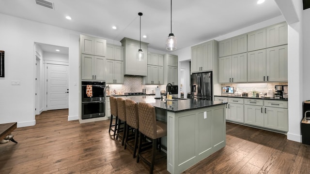 kitchen with dark wood-type flooring, stainless steel appliances, an island with sink, decorative light fixtures, and gray cabinets