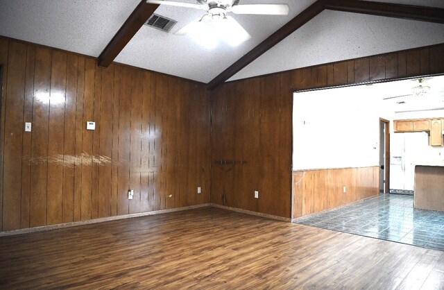 spare room with ceiling fan, lofted ceiling with beams, wood walls, hardwood / wood-style floors, and a textured ceiling