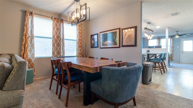 dining area featuring a textured ceiling, light carpet, a wealth of natural light, and ceiling fan with notable chandelier