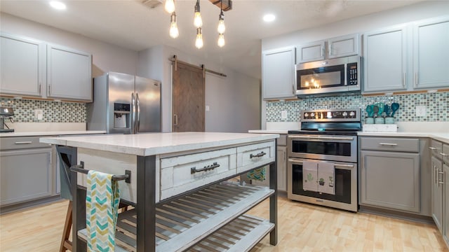 kitchen featuring appliances with stainless steel finishes, gray cabinets, a barn door, and tasteful backsplash