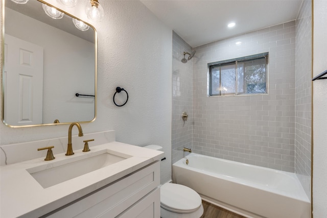 full bathroom featuring vanity, hardwood / wood-style floors, tiled shower / bath, and toilet