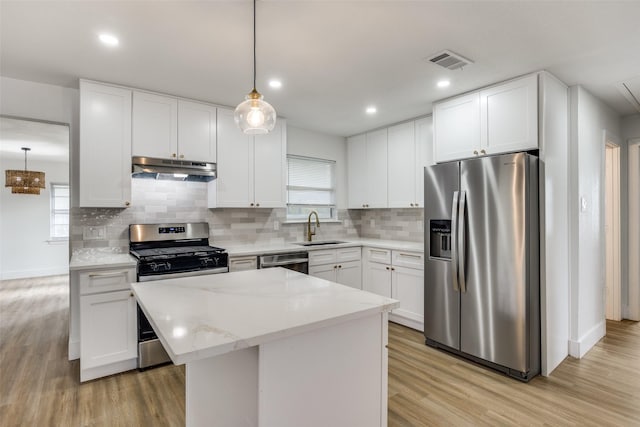 kitchen with white cabinets, hanging light fixtures, a kitchen island, appliances with stainless steel finishes, and light hardwood / wood-style floors