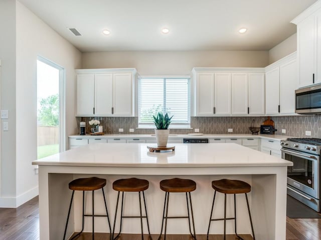 kitchen with white cabinets, appliances with stainless steel finishes, backsplash, and a kitchen island