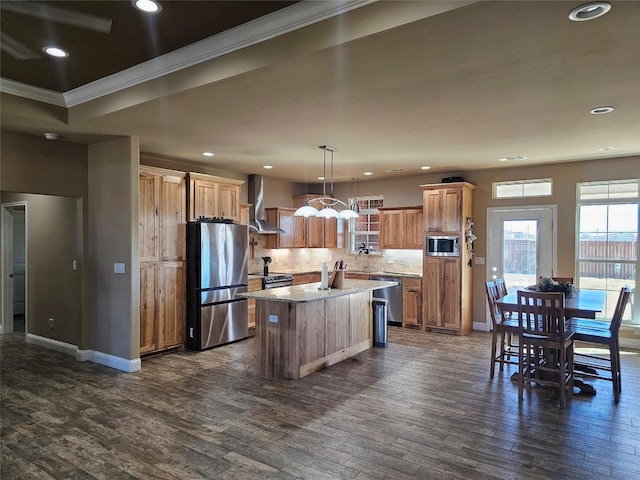 kitchen featuring dark wood-type flooring, wall chimney exhaust hood, decorative light fixtures, a kitchen island, and stainless steel appliances