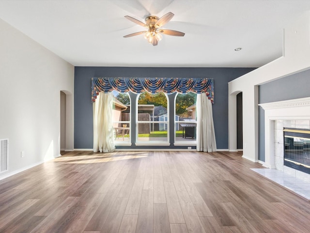 unfurnished living room with a tiled fireplace, ceiling fan, and wood-type flooring