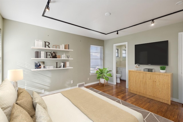 bedroom featuring track lighting, ensuite bath, and dark wood-type flooring