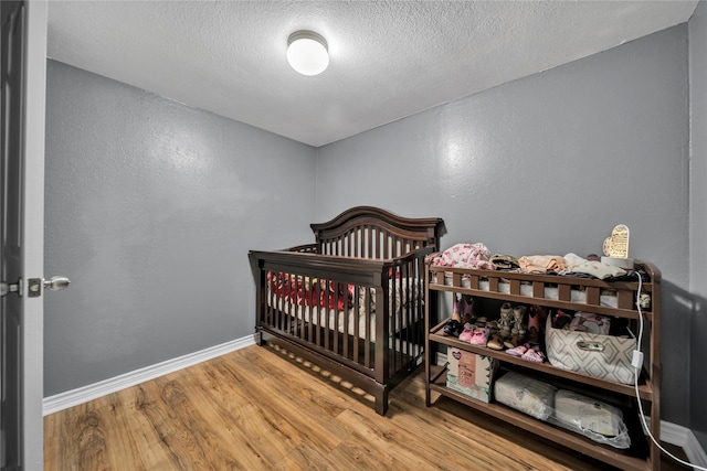 bedroom with hardwood / wood-style floors, a nursery area, and a textured ceiling