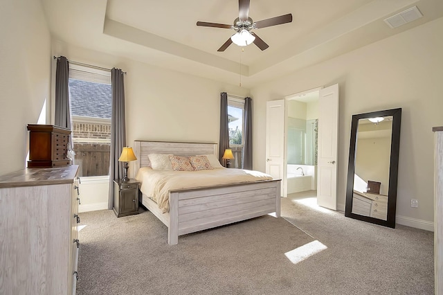 carpeted bedroom featuring a raised ceiling, ensuite bath, and ceiling fan