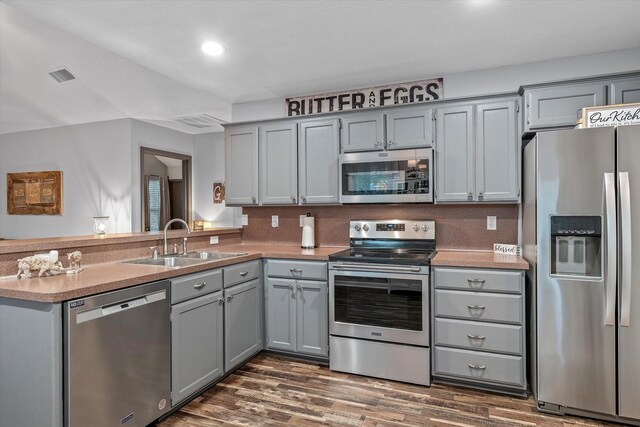 kitchen with kitchen peninsula, appliances with stainless steel finishes, dark hardwood / wood-style flooring, sink, and gray cabinets