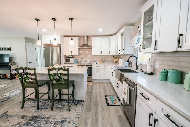 kitchen featuring wall chimney range hood, a kitchen breakfast bar, light hardwood / wood-style flooring, white cabinets, and appliances with stainless steel finishes