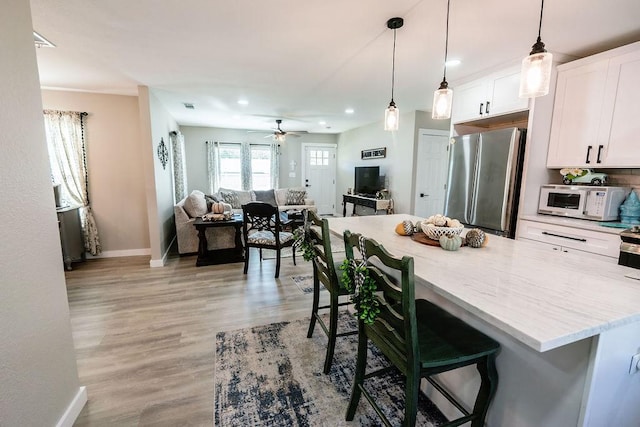 kitchen featuring white cabinets, a breakfast bar, stainless steel refrigerator, and hanging light fixtures