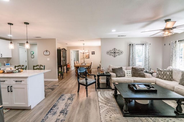 living room featuring ceiling fan with notable chandelier and light wood-type flooring