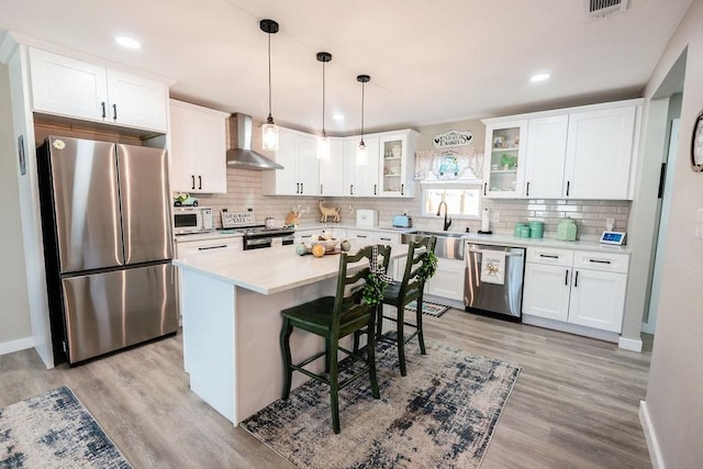 kitchen featuring stainless steel appliances, white cabinetry, a kitchen island, and wall chimney range hood