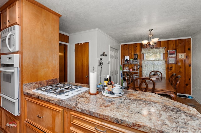 kitchen with ornamental molding, white appliances, a notable chandelier, light stone countertops, and a textured ceiling