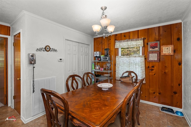 dining space featuring ornamental molding, wooden walls, a textured ceiling, and a notable chandelier