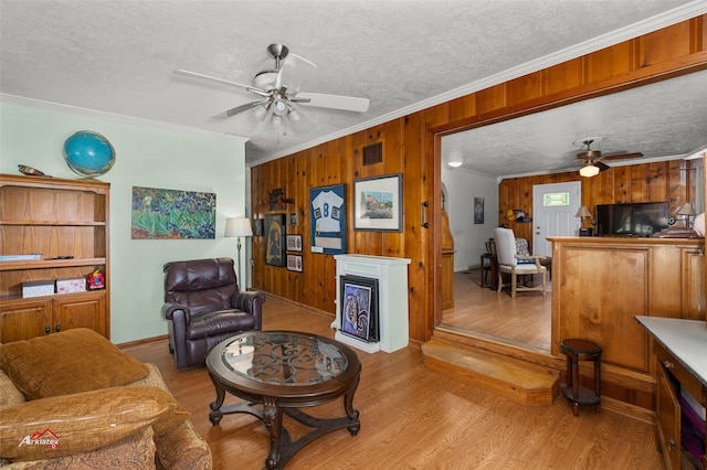 living room with light hardwood / wood-style flooring, ceiling fan, wooden walls, ornamental molding, and a textured ceiling