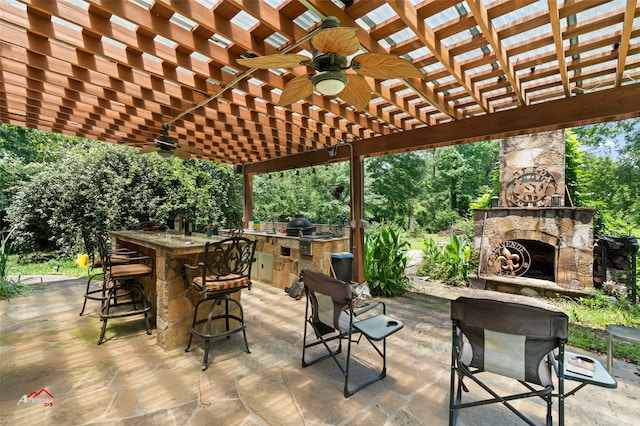 view of patio / terrace with a pergola, a bar, ceiling fan, exterior kitchen, and an outdoor stone fireplace