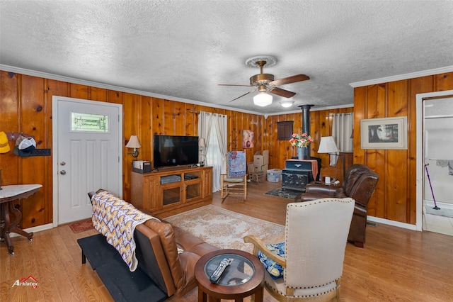 living room featuring crown molding, ceiling fan, light hardwood / wood-style floors, a textured ceiling, and a wood stove