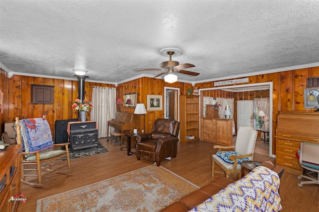 living room with light hardwood / wood-style flooring, wooden walls, ornamental molding, a textured ceiling, and a wood stove