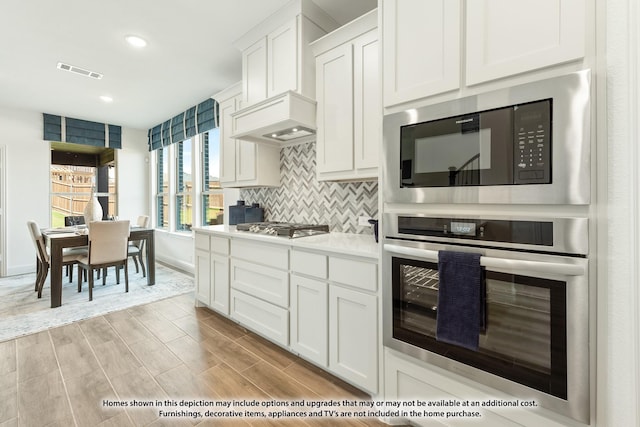 kitchen featuring appliances with stainless steel finishes, backsplash, white cabinetry, and light hardwood / wood-style flooring