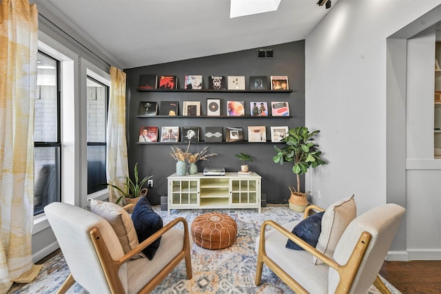 sitting room with hardwood / wood-style floors and vaulted ceiling with skylight