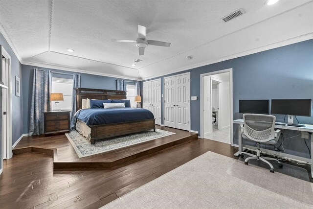 bedroom with two closets, ceiling fan, ornamental molding, a textured ceiling, and dark hardwood / wood-style flooring