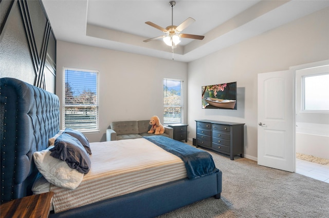 bedroom with ceiling fan, light colored carpet, a tray ceiling, and multiple windows