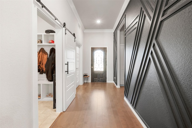 mudroom with a barn door, ornamental molding, and light hardwood / wood-style flooring