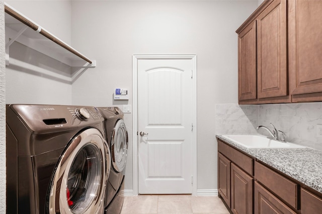 laundry area featuring washing machine and clothes dryer, sink, light tile patterned floors, and cabinets