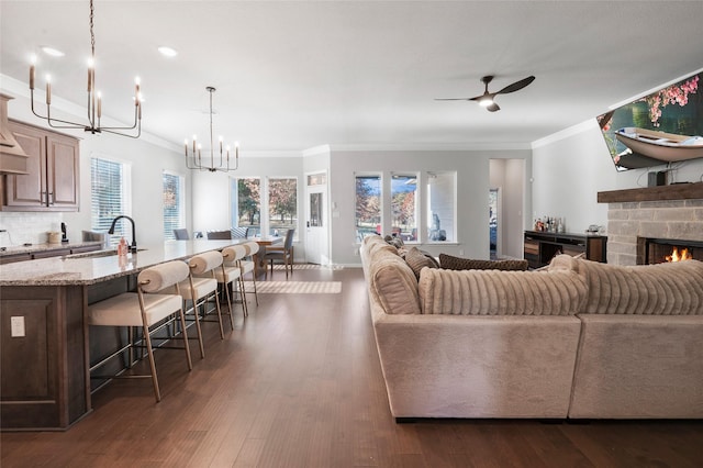 living room featuring crown molding, dark hardwood / wood-style flooring, ceiling fan with notable chandelier, and sink