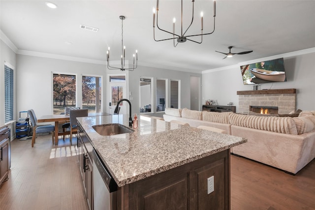 kitchen with a fireplace, an island with sink, decorative light fixtures, and sink