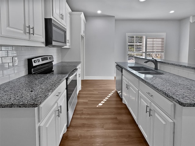 kitchen featuring appliances with stainless steel finishes, dark stone counters, sink, dark hardwood / wood-style floors, and white cabinetry