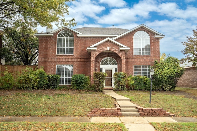 traditional-style home featuring a front yard, brick siding, fence, and a chimney