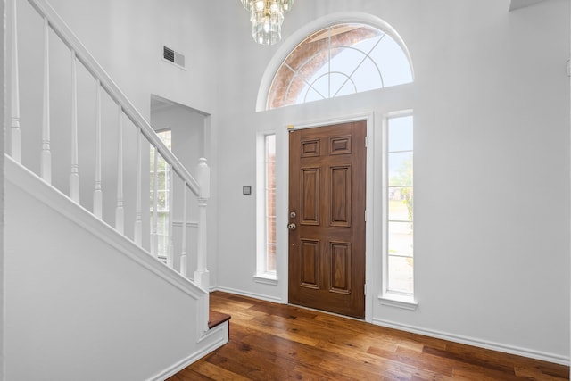 foyer with visible vents, stairway, a towering ceiling, a chandelier, and hardwood / wood-style flooring