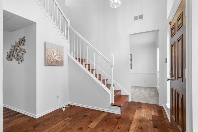 foyer entrance with visible vents, hardwood / wood-style floors, a high ceiling, baseboards, and stairs