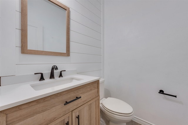 bathroom with vanity, toilet, and wood walls